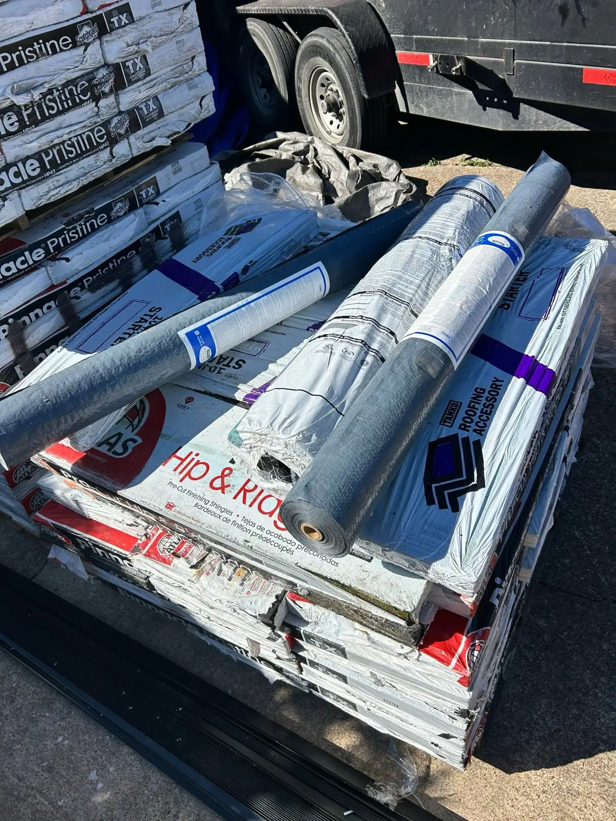 February 23. The spec on the driveway — Atlas Pinnacle Pristine wrappers, hip-and-ridge, and underlayment rolls on the pallet.